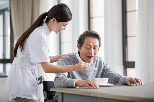 alt text: Hình ảnh điều dưỡng đang chăm sóc bệnh nhân cao tuổi ngồi trên xe lăn